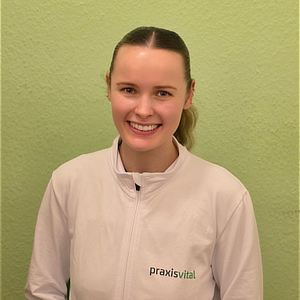 Junge Frau mit Zopf lächelt freundlich vor grüner Wand und trägt weiße Jacke