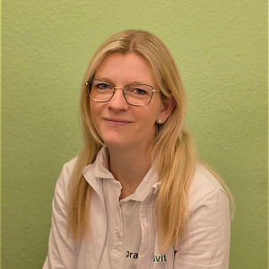 Blonde Frau mit Brille lächelt freundlich vor grünem Hintergrund in weißem Hemd